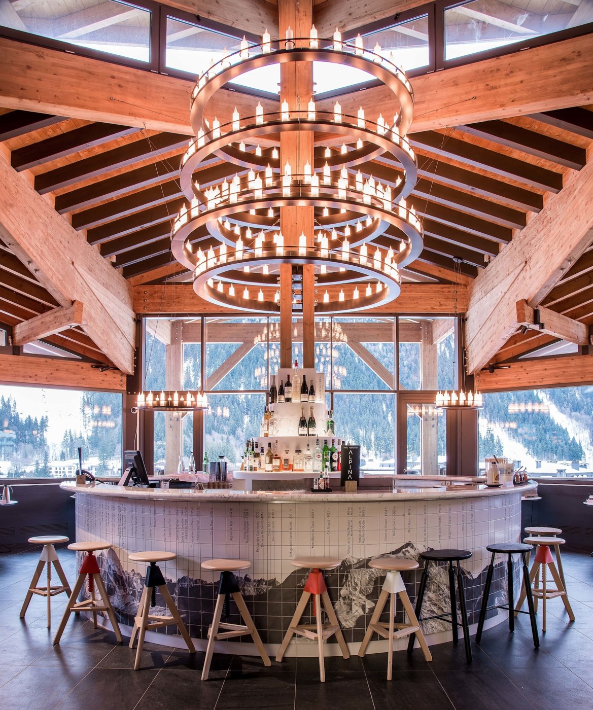 A bar with a circular chandelier, wooden beams, and a view of mountains through large windows. - Alpina Eclectic Hotel (Chamonix-Mont-Blanc)